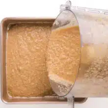 Cake batter is being poured from a food processor into a square cake pan.