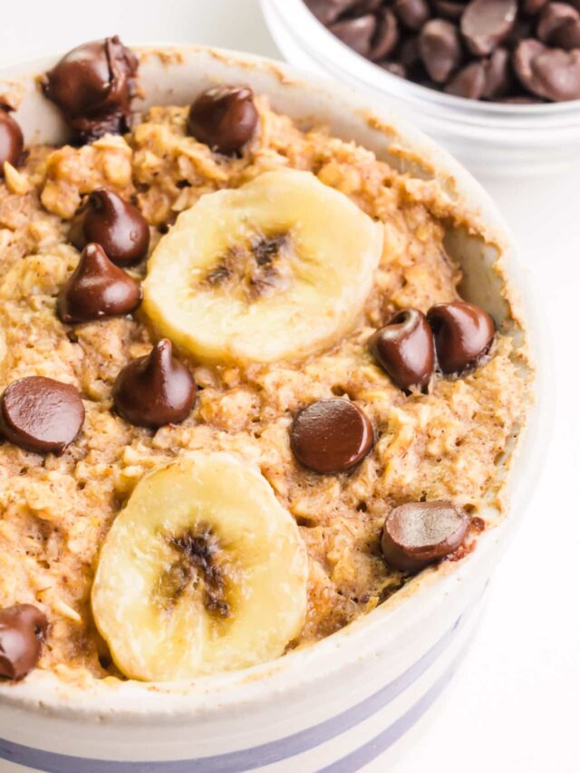 A bowl of vegan baked oats has chocolate chips and banana slices on top. There is a bowl of chocolate chips in the background.
