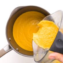 Cheese sauce is being transferred from a blender to a saucepan.