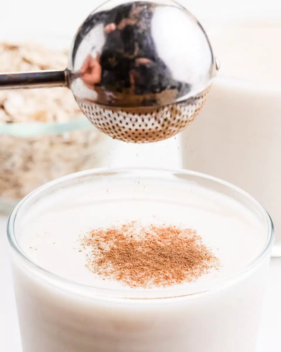 Spices are being sprinkled over a glass of oat milk.