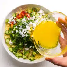 Salad dressing is being poured over a salad with lots of veggies.