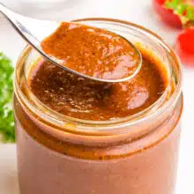A spoonful of enchilada sauce hovers over a jar with more of the sauce.