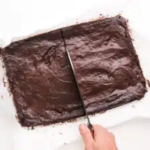 A knife cuts a long rectangle chocolate cookie in half.