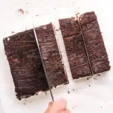 A knife is being used to cut big blocks of ice cream sandwiches into smaller sandwiches.