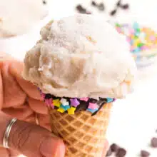 A hand holds an ice cream cone with vegan vanilla ice cream on it.