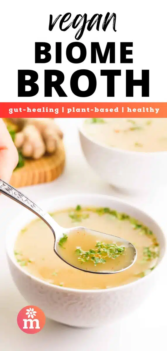 A spoonful of broth hovers over a bowl. There is another bowl of broth and fresh ginger in the background. The text reads, Vegan Biome Broth, gut-healing, plant-based, healthy.