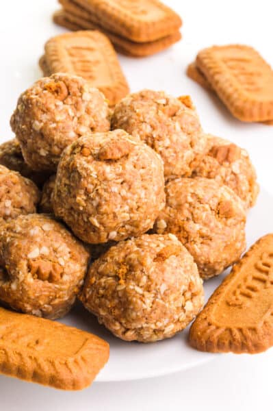 A stack of vegan Biscoff protein balls sit on a plate around some Biscoff cookies.