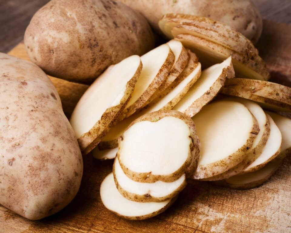 A photo of russet potatoes on a cutting board, some of them are sliced.