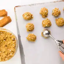 A hand holds a cookie dough dispenser pressing cookie dough balls on a baking pan.