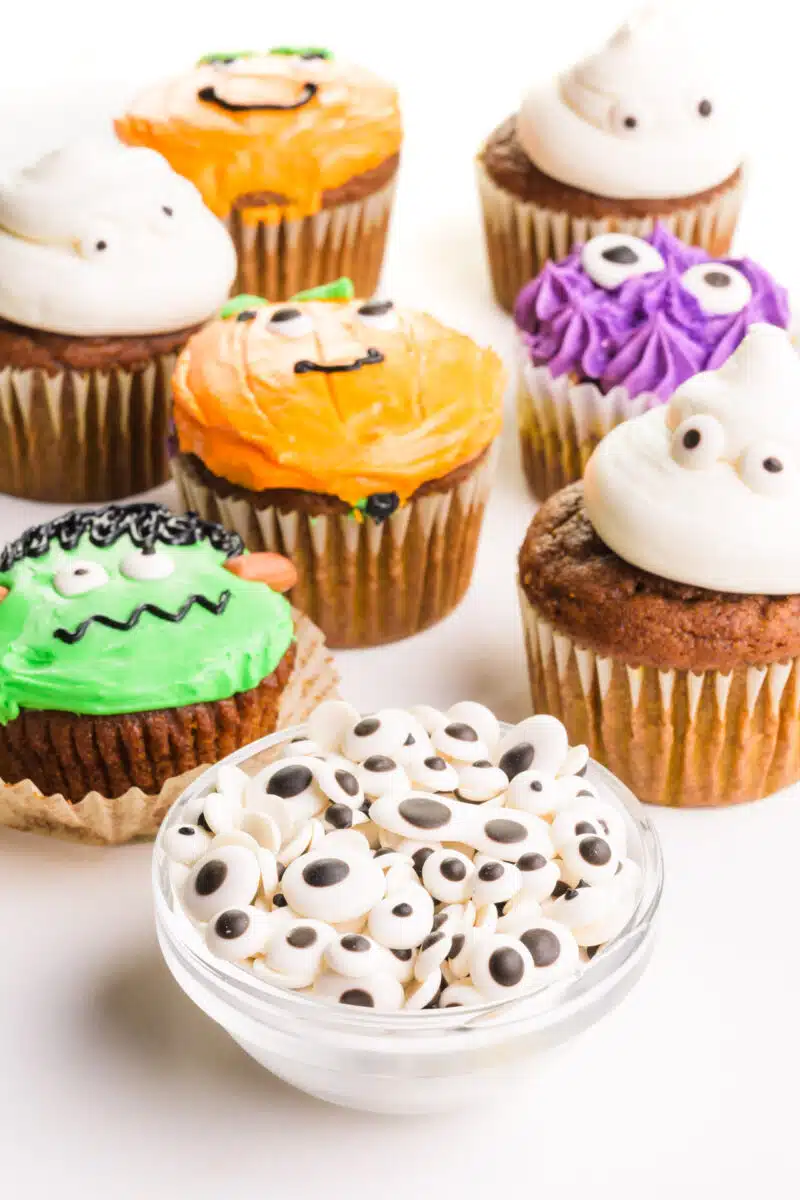 A bowl of vegan googly eyes sits in front of Halloween cupcakes decorated with the candies.