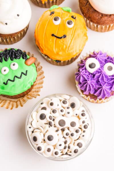 Looking down on a bowl of candy eyes surrounded by Halloween cupcakes with candy eyes on each of them.