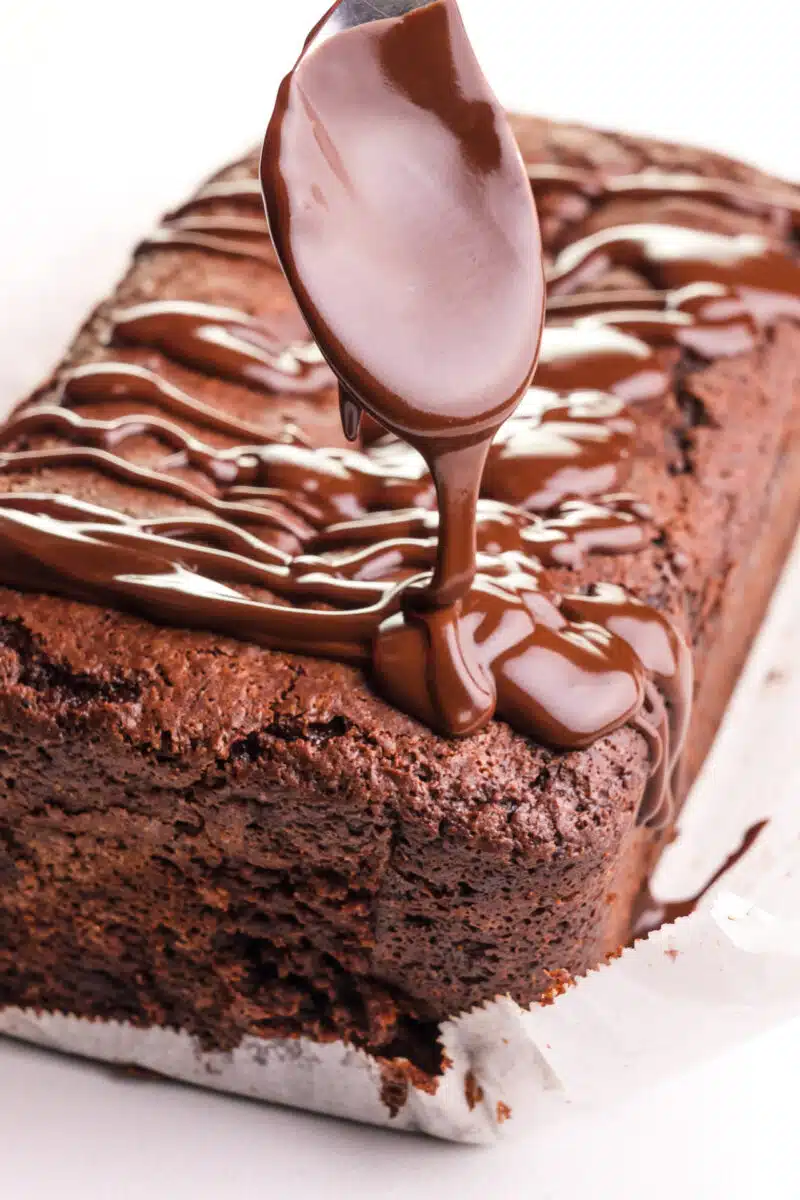 A spoon drizzles chocolate sauce over a vegan chocolate loaf.