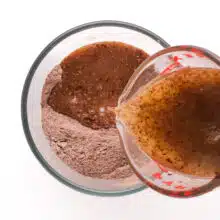 A chocolate mixture is being poured into a mixing bowl with flour and cocoa ingredients.