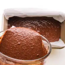Chocolate batter is being poured from a bowl into a loaf pan.