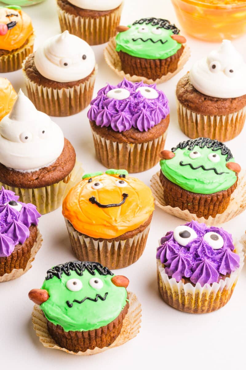 A bunch of colorful Halloween cupcakes on a table, including purple monsters and white ghosts.