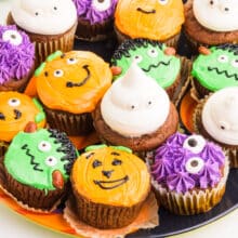 A plate holds several Vegan Halloween Cupcakes decorated in different colors and styles.