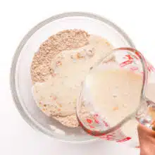 A plant-based milk mixture is being poured into a bowl with flour.