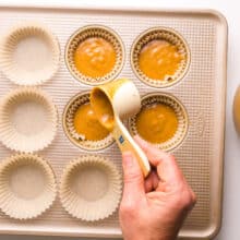 A hand pours pumpkin batter into muffin pan compartments.