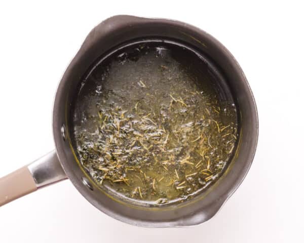 Melted butter is in a saucepan with herbs.