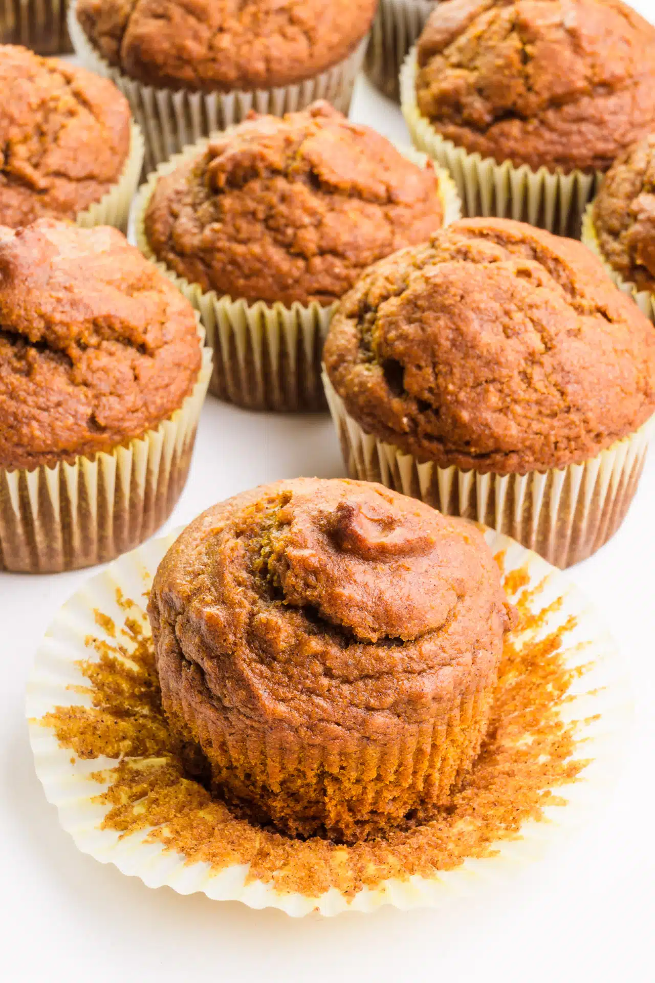 A vegan pumpkin muffin sits in front of more pumpkin muffins.
