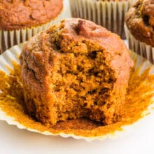 An egg-free pumpkin muffin has a bite taken out. It sits in front of more muffins in the background.