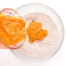 A pumpkin mixture is being poured into a bowl with flour mixture.