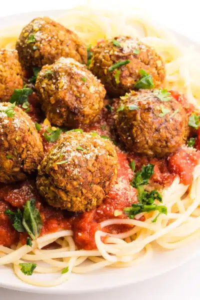 A plate of pasta has marinara sauce and chickpea balls on top.