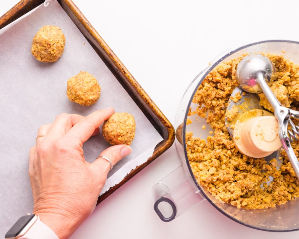 A hand places a chickpea meatball on a prepared baking pan.