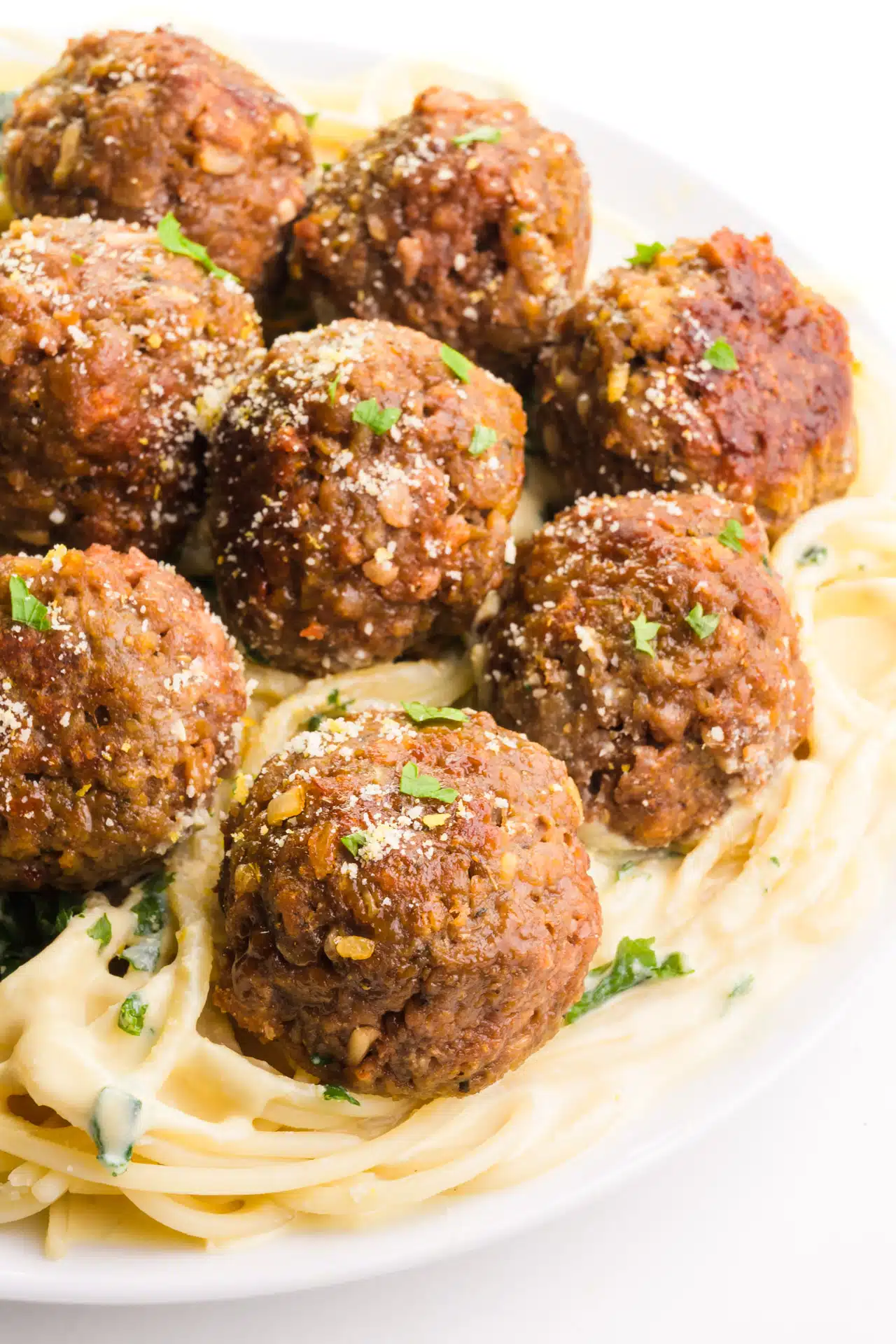 A delectable plate of pasta adorned with creamy sauce, crowned with several succulent Impossible Burger Meatballs. A mouthwatering and indulgent plant-based feast.