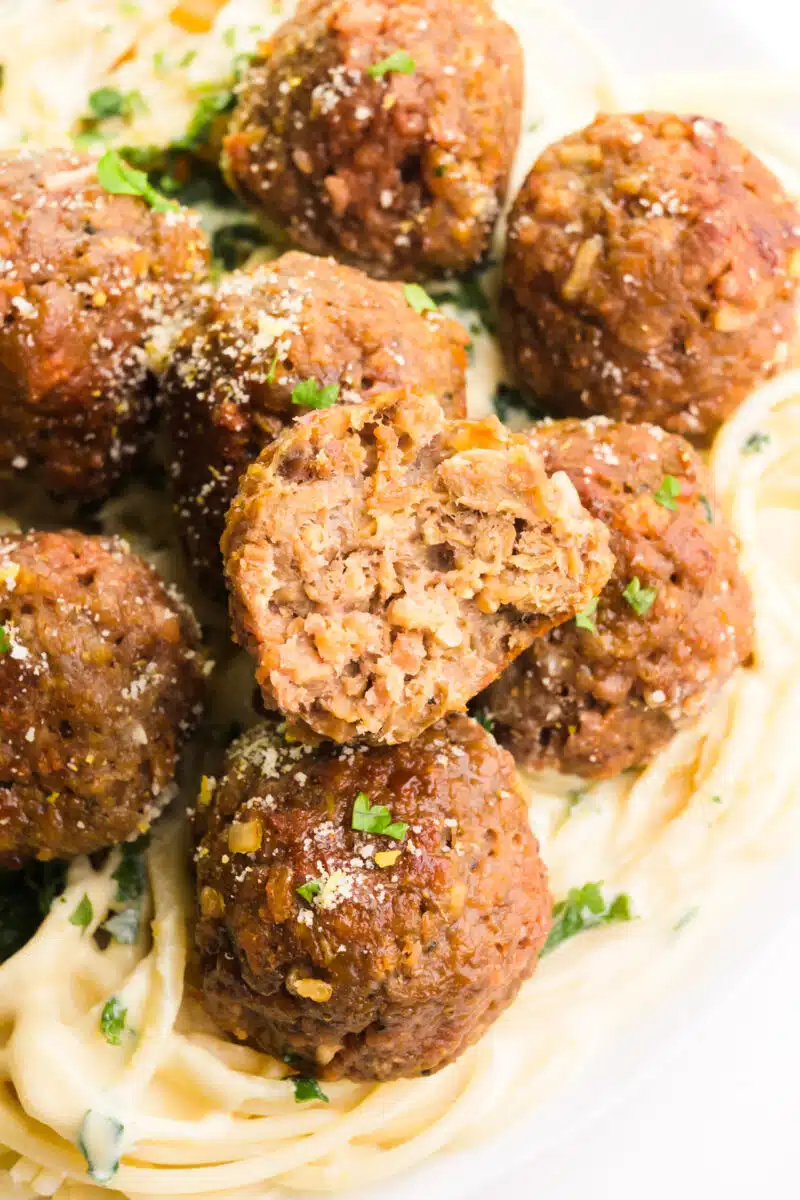 A delicious stack of Impossible Meat meatballs atop a generous serving of pasta. The top meatball proudly displays a tempting bite taken out, showcasing the mouthwatering texture and flavor of these plant-based delights.