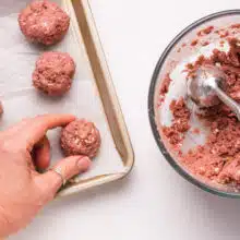 Hands at work in the kitchen as uncooked Impossible Burger meatballs are carefully placed on a baking sheet. A bowl filled with the flavorful meatball mixture and a convenient dispenser sit nearby, highlighting the easy and enjoyable process of preparing these plant-based delights.