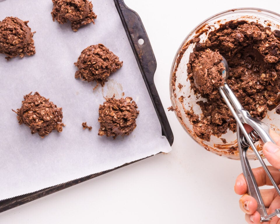 Hand scooping cookie batter onto parchment-lined baking sheet with several other cookies.
