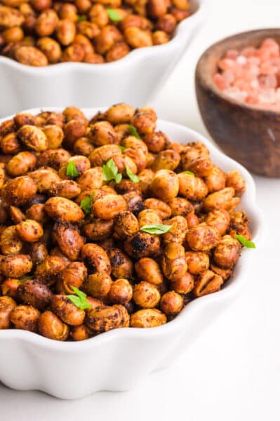 A bowl of roasted soybeans sits in front of spices and another bowl of the snack.