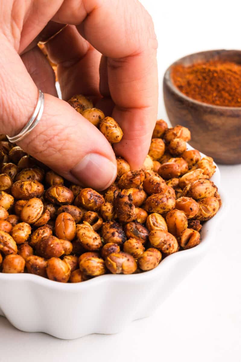 A hand reaches into a bowl of roasted soybeans. There is a bowl of spices in the background.