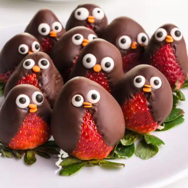 A plate full of strawberry penguins sit on a plate.