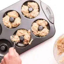 Batter is being distributed from a mixing bowl into a donut pan.