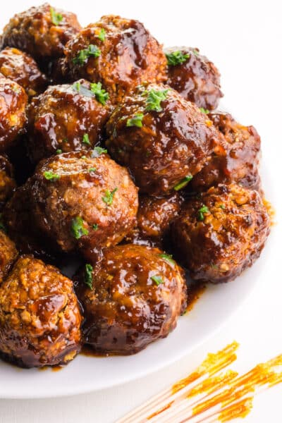 A plate of vegan grape jelly meatballs sits on a plate in front of toothpicks.