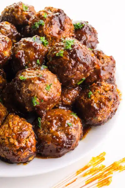A plate of vegan grape jelly meatballs sits on a plate in front of toothpicks.