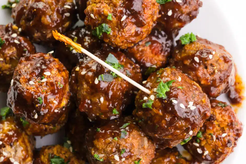 Looking down on a plate of vegan meatballs, one is skewered with a toothpick.