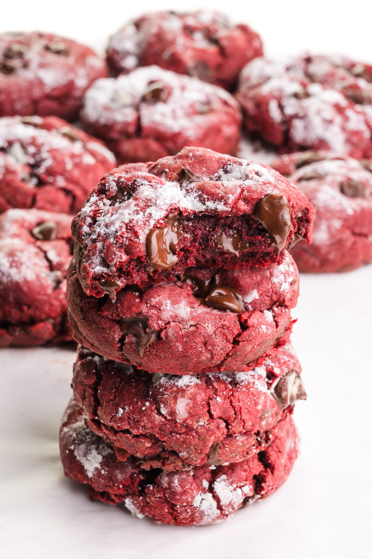 A stack of vegan red velvet cookies shows the top one with a bite taken out. There are more cookies in the background.