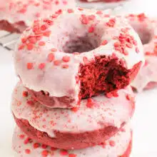 A stack of vegan red velvet doughnuts shows the top one with a bite taken out.