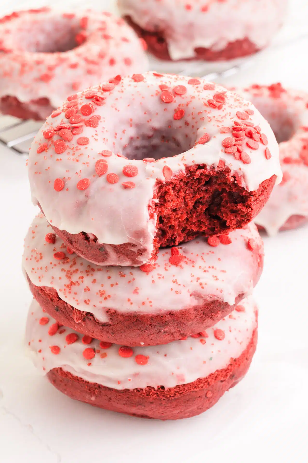 A stack of red velvet donuts shows the top one with a bite taken out.