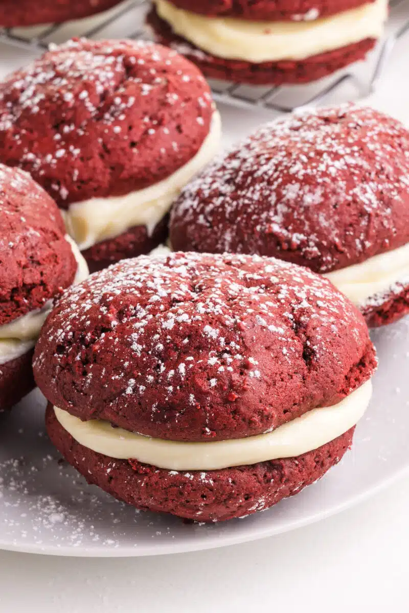 Several vegan red velvet whoopie pies on a plate. There are more in the background.