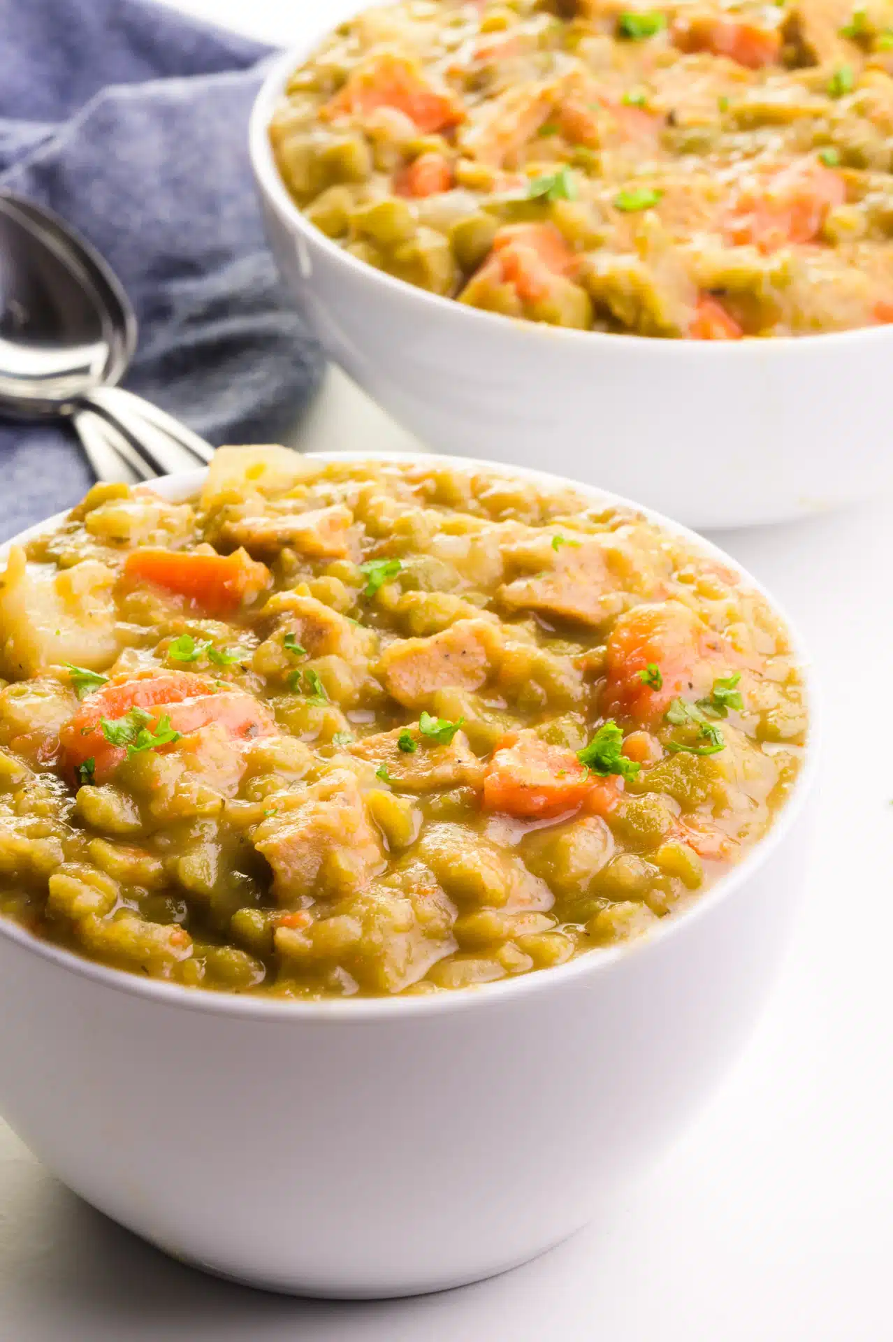 A bowl of vegan split pea soup sits in front of a kitchen towel and a second bowl of the soup.