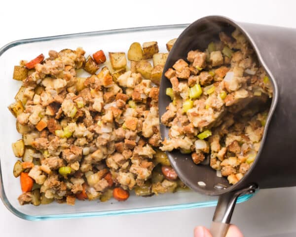 Stuffing is being poured from a saucepan into a baking dish.