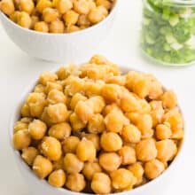 Two bowls of chickpeas sit on a counter next to a jar of chopped green onions.