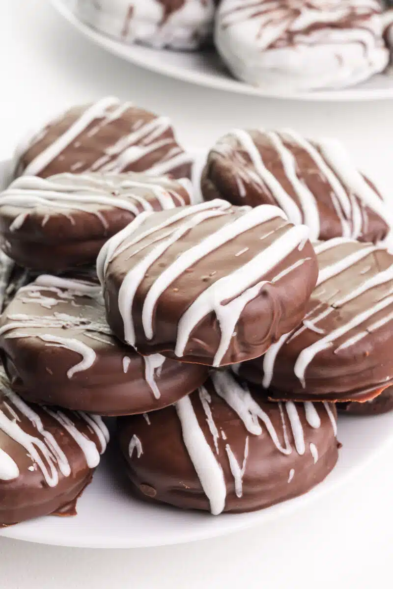 Dairy-free chocolate-covered Oreos sit on a plate. There are more on a plate in the background.