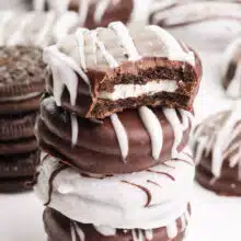 A stack of vegan chocolate-covered Oreos shows the top one with a bite taken out.