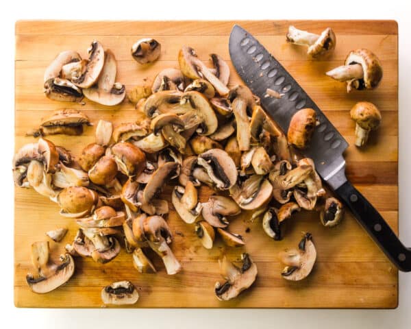Looking down on some whole and chopped mushrooms on a cutting board with a knife.