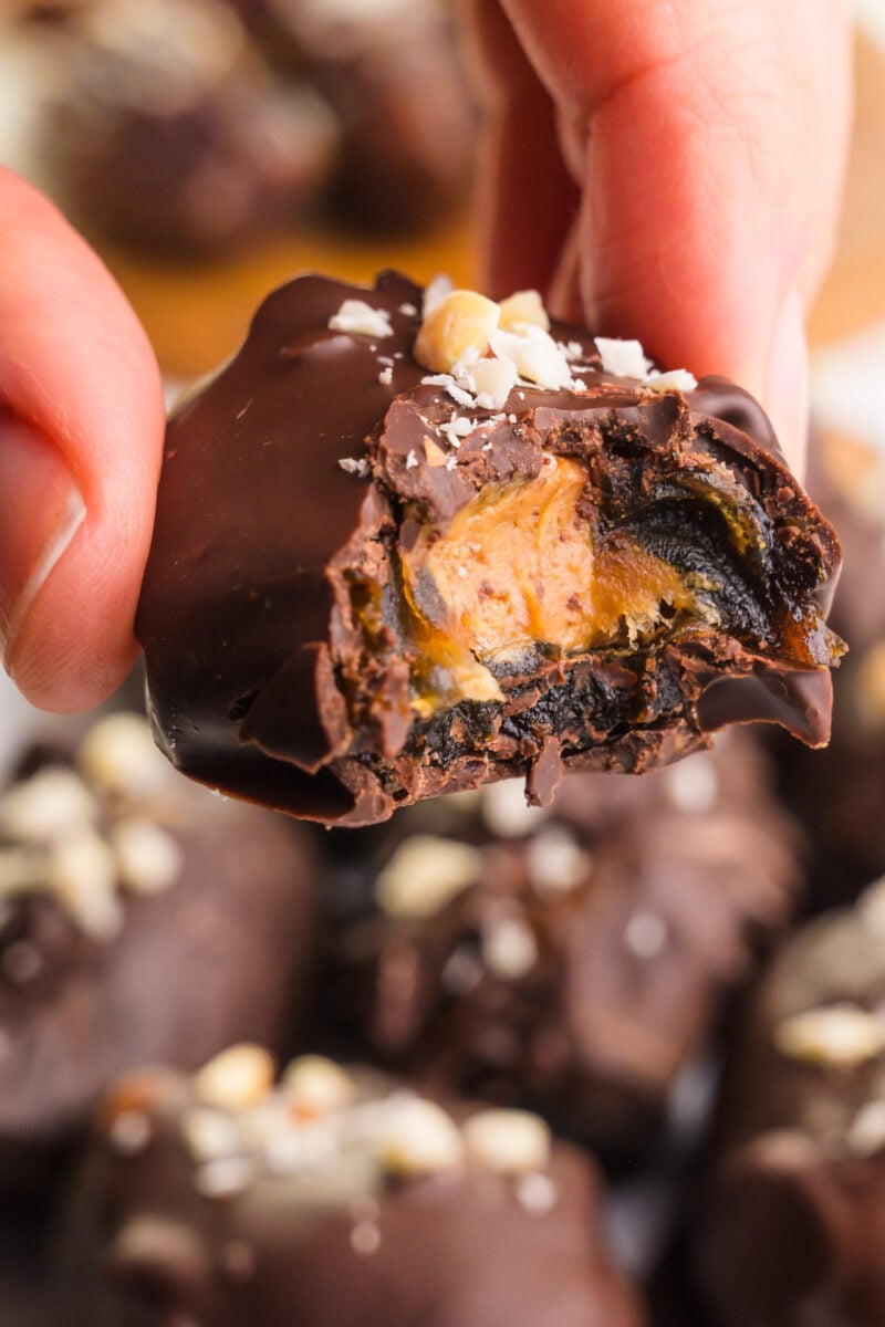 A hand holds a date snickers treat with a bite taken out.